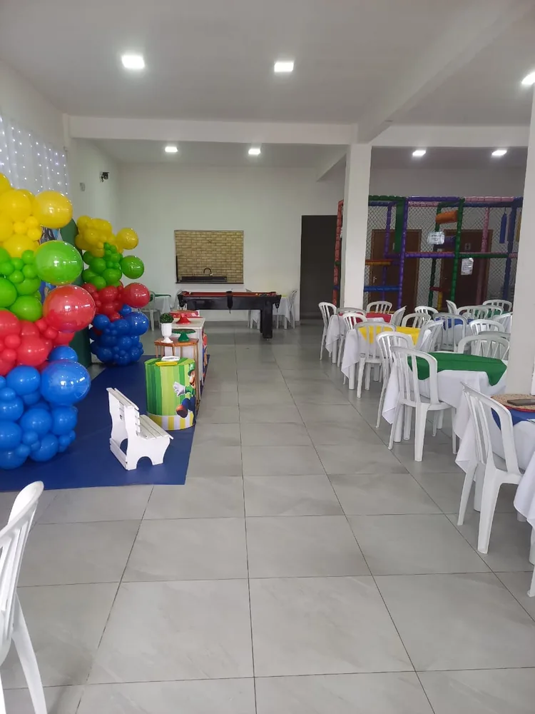 Salão amplo com mesas, decoração de balões e playground ao fundo